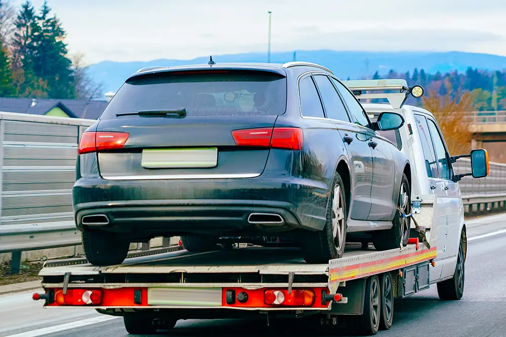 A flatbed recovery truck carrying a car along a highway