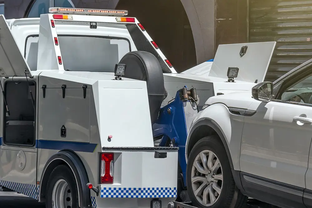 A wheel-lift tow truck lifting an SUV on a city street